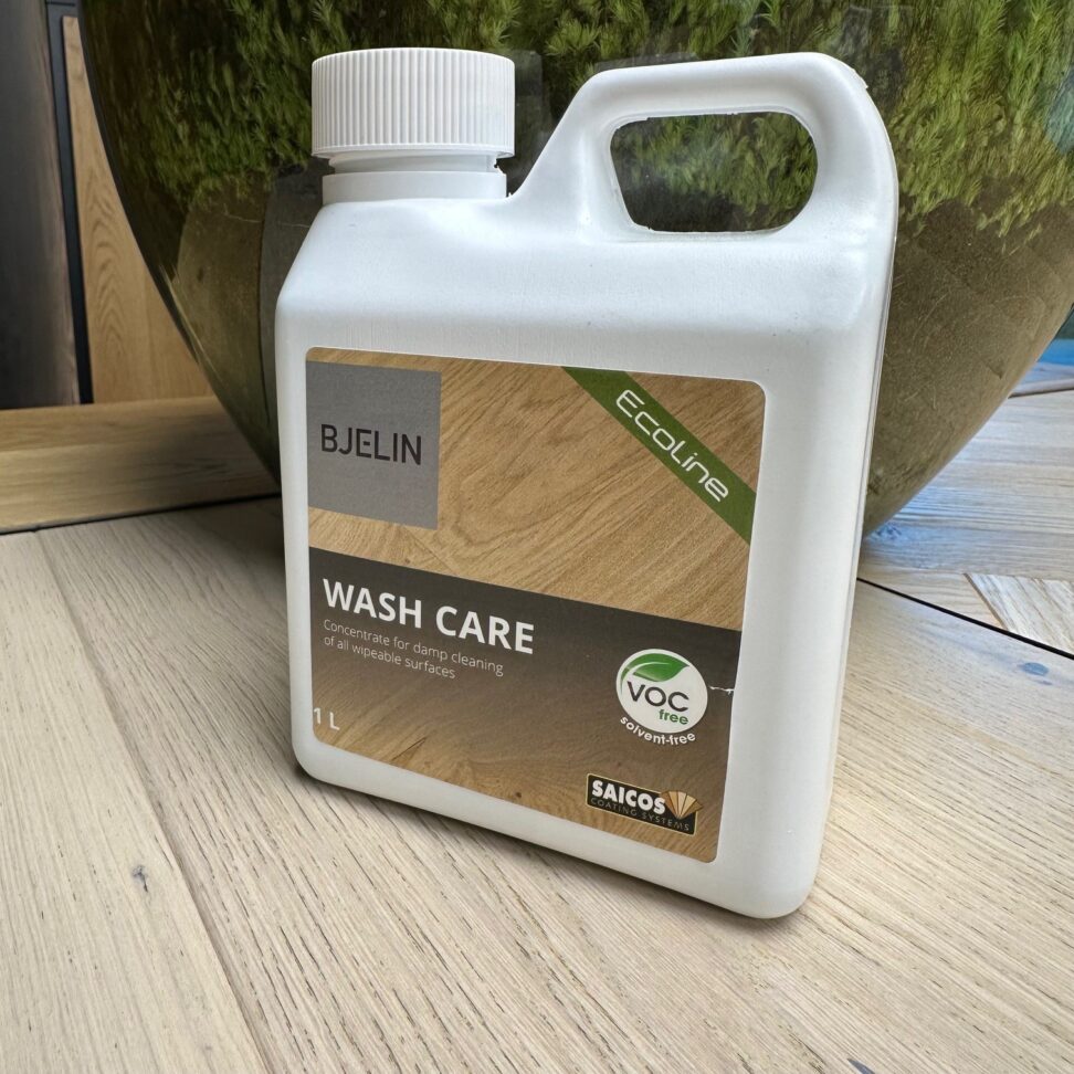 White bottle of BJELIN Wash Care on a wooden surface with a blurred green plant in the background
