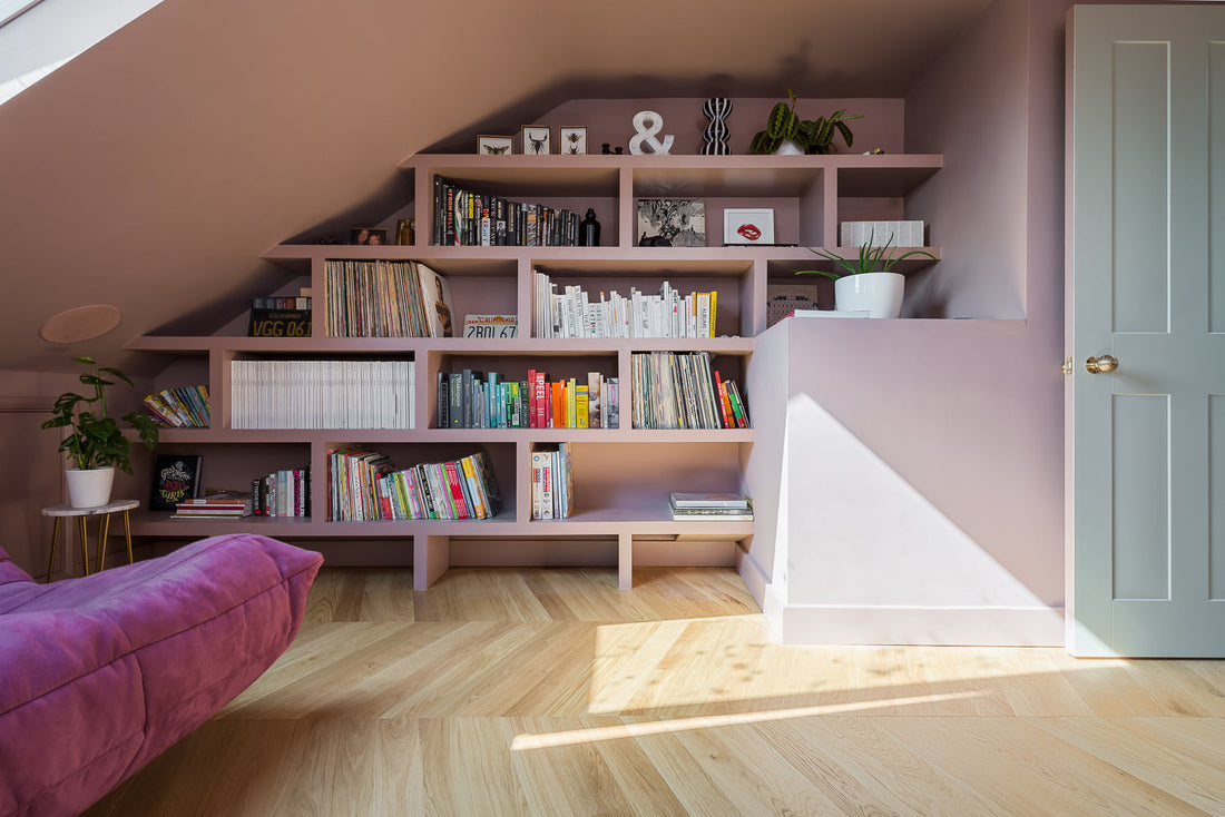 cosy loft room with pink bookshelf and velvet sofa and chevron flooring
