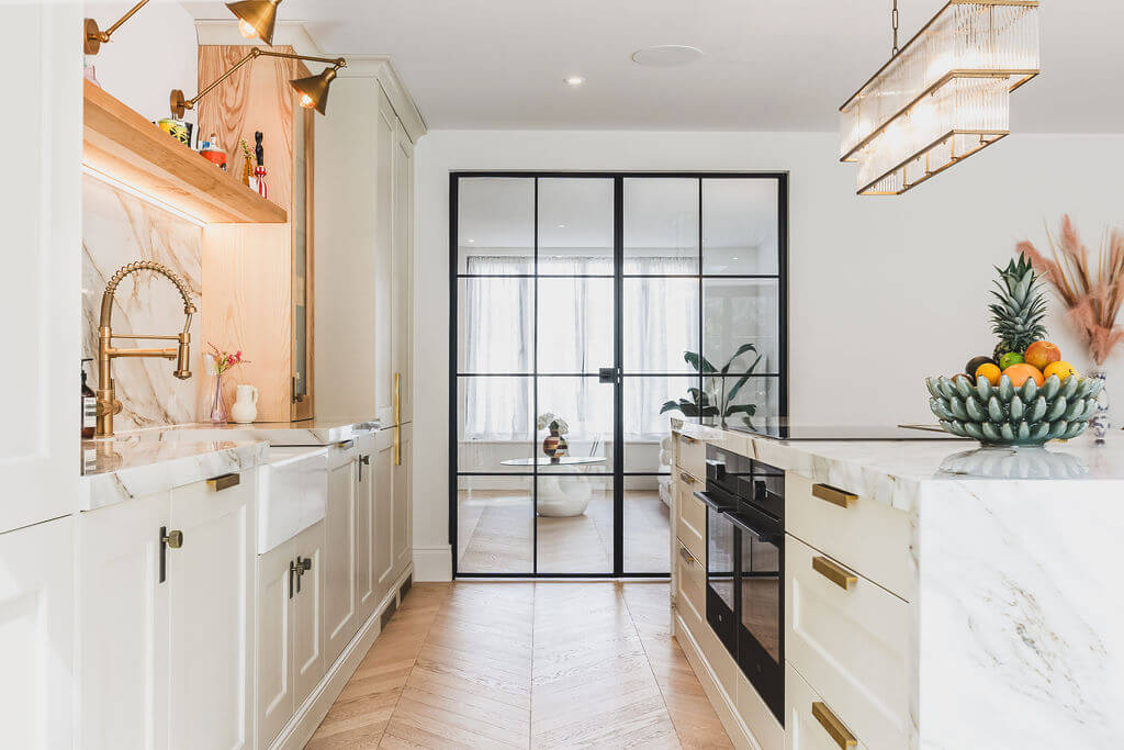 looking through a kitchen with crittall doors leading to a living room and chevron oak wood flooring