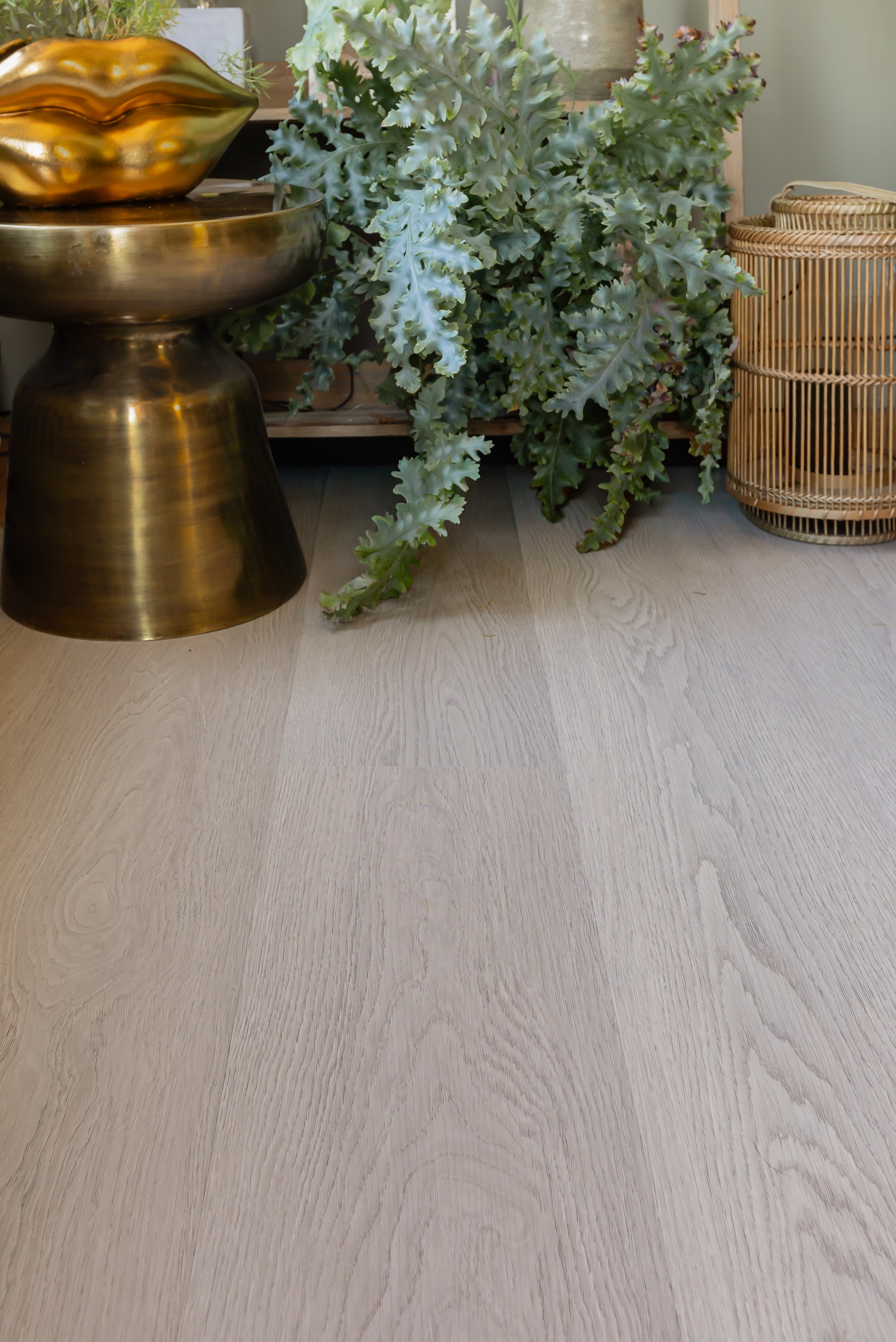 Mid-tone oak SPC vinyl floor with decorative elements including a gold bowl, plants, and a woven basket.