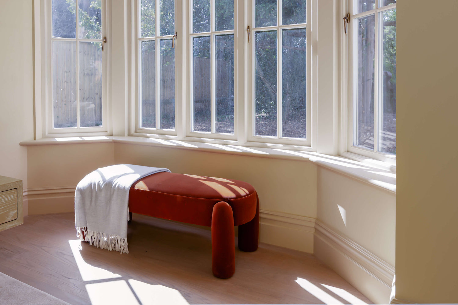 Sunlight coming through a bay window onto an orange footstool and wood floors