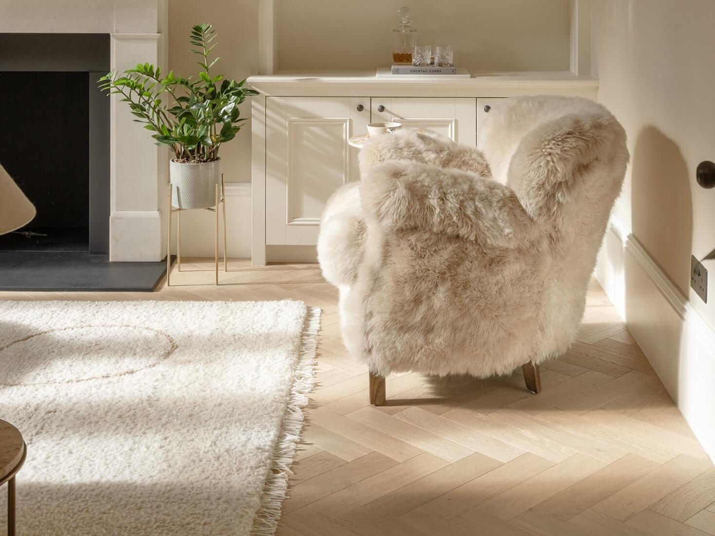 Fluffy white armchair in a stylish living room with a fireplace and Shore Drift Oak herringbone floors