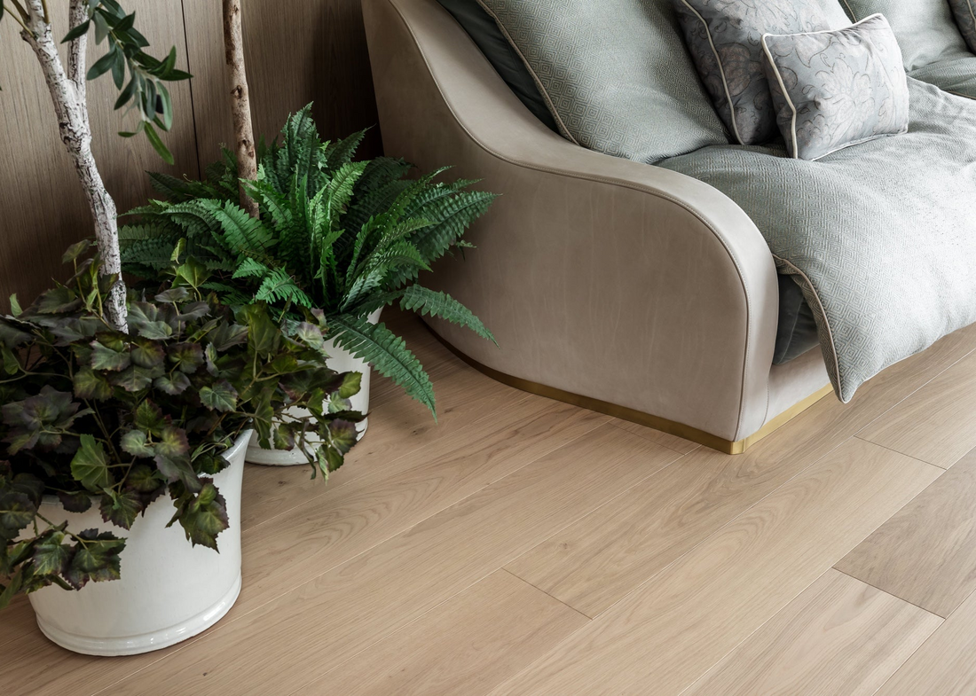 Potted plants on a wooden floor next to a gray sofa