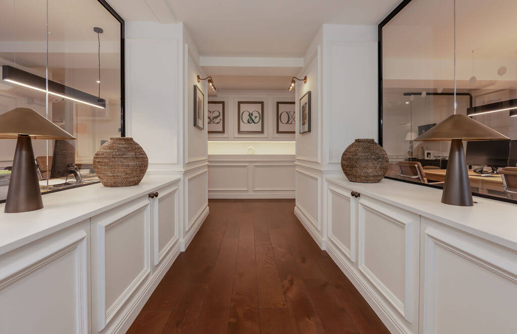 An office design with white paneled walls and counters, dark wood flooring, pendant lights, framed wall art, and decorative woven vases.