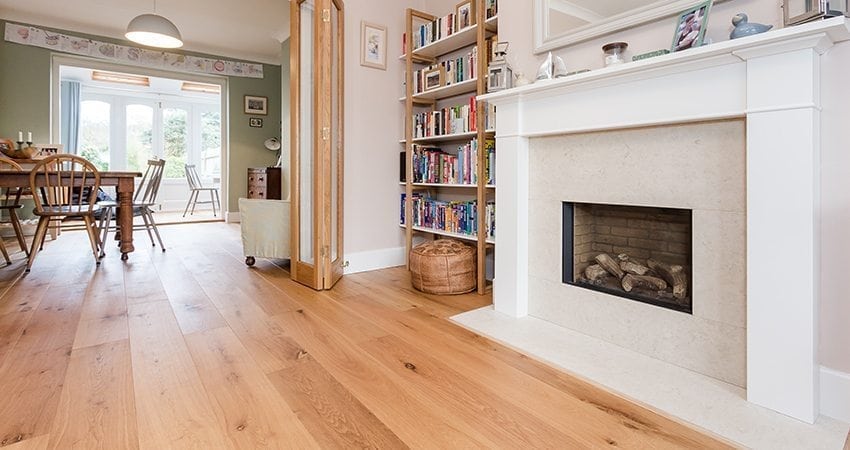 Large oak wood flooring planks in a living room with a large marble fireplace