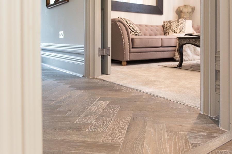 herringbone oak wood floor in a hallway, with a softly furnished room in the background