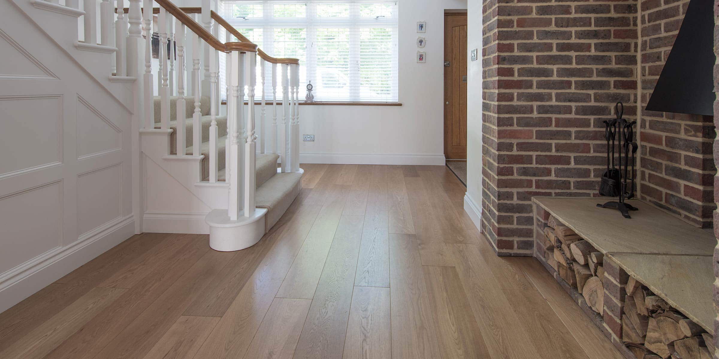 Alpine wide plank oak floors in a hallway with a staircase on the left and brick will on the right