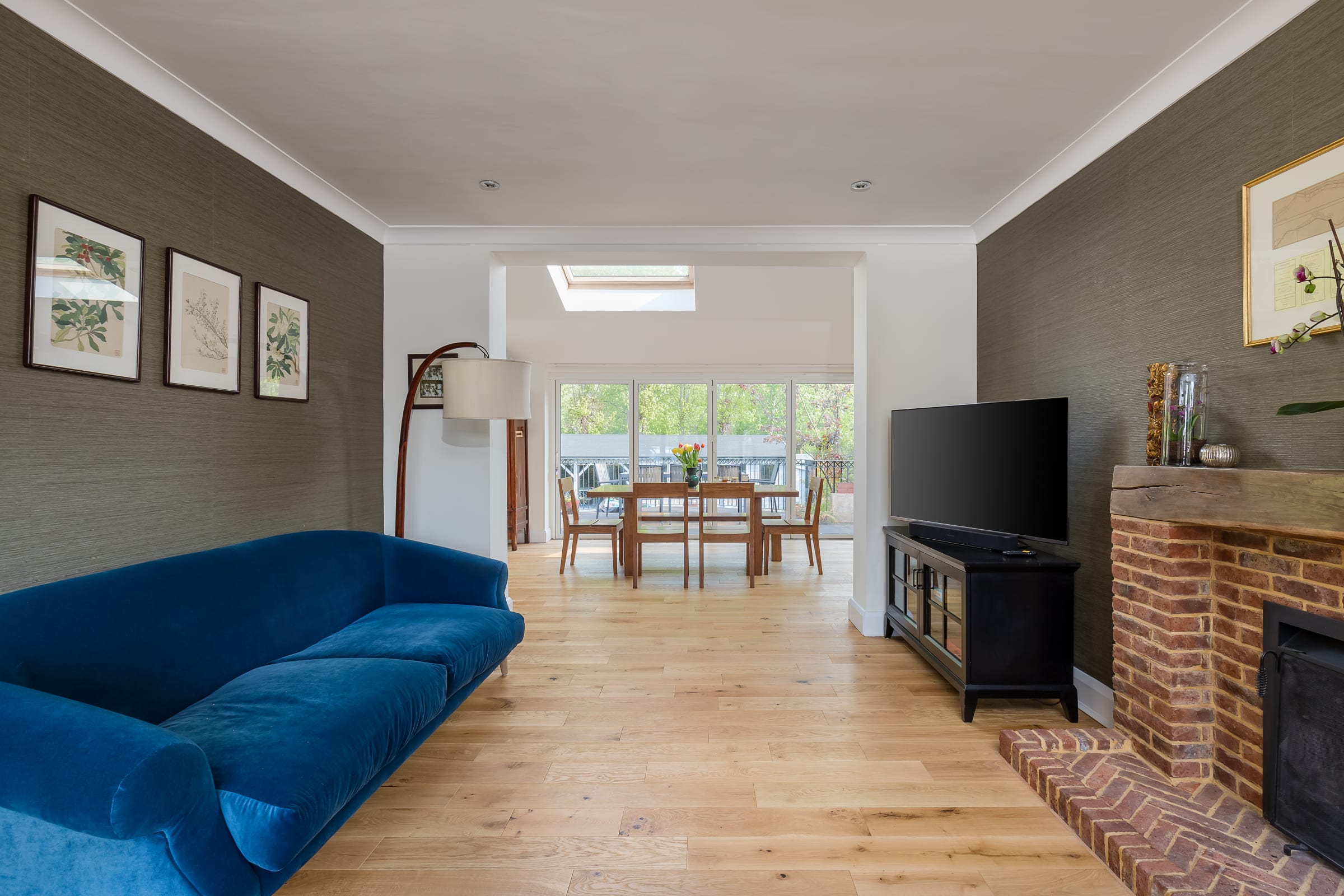 long view of a living room with light wood floors, a blue couch, and a wooden dining table