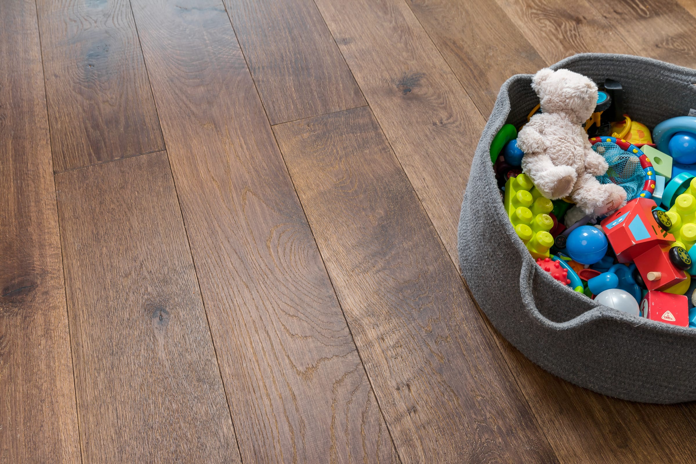 close up of dark wood floors with a basket of toys on the right