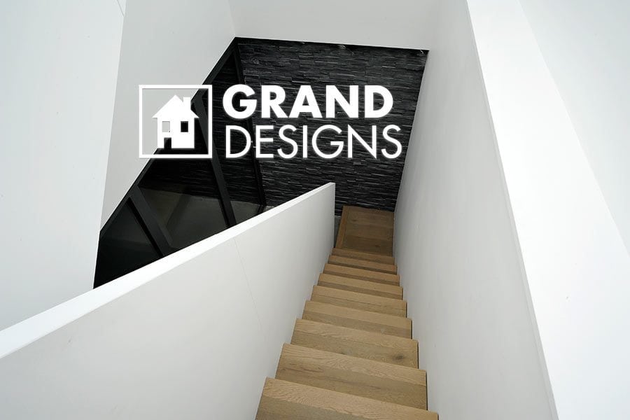 Modern white walled stairwell with oak wood stairs, featuring the Grand Designs logo