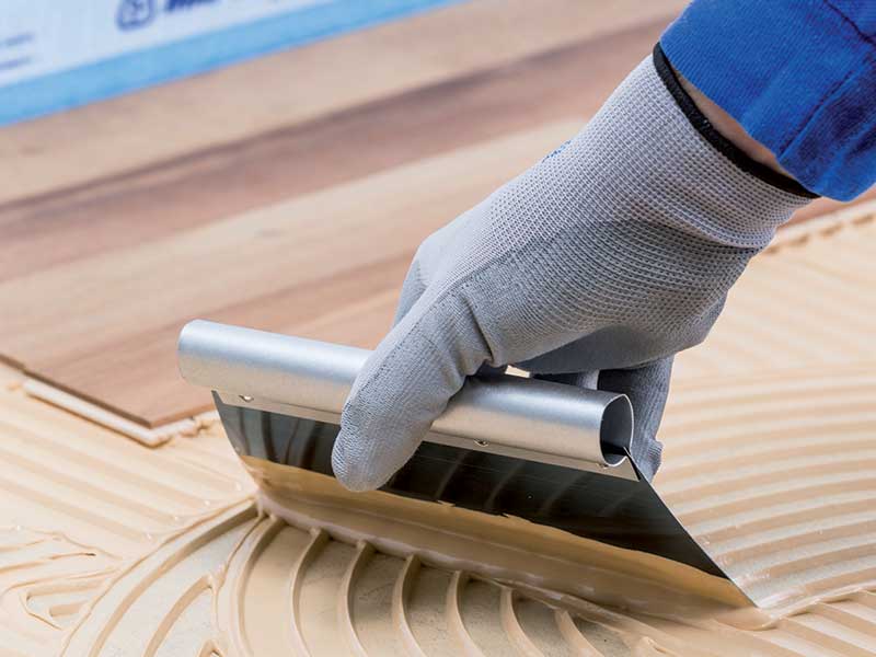 close up of a person wearing gloves, spreading adhesive onto wood floors