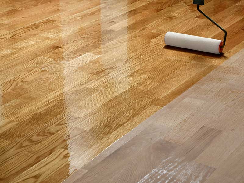 a roller applying shiny lacquer to wood floors