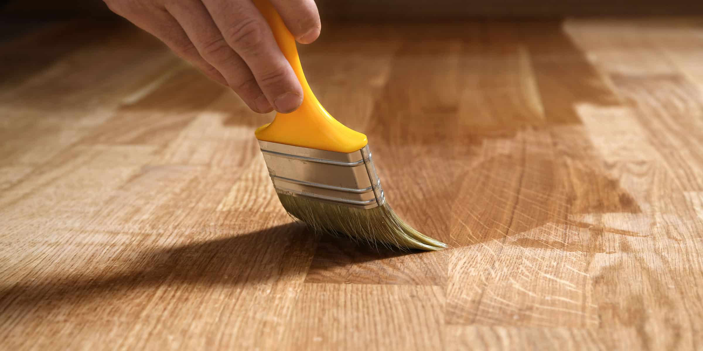 a person brushing oil onto oak floors, wood floor care