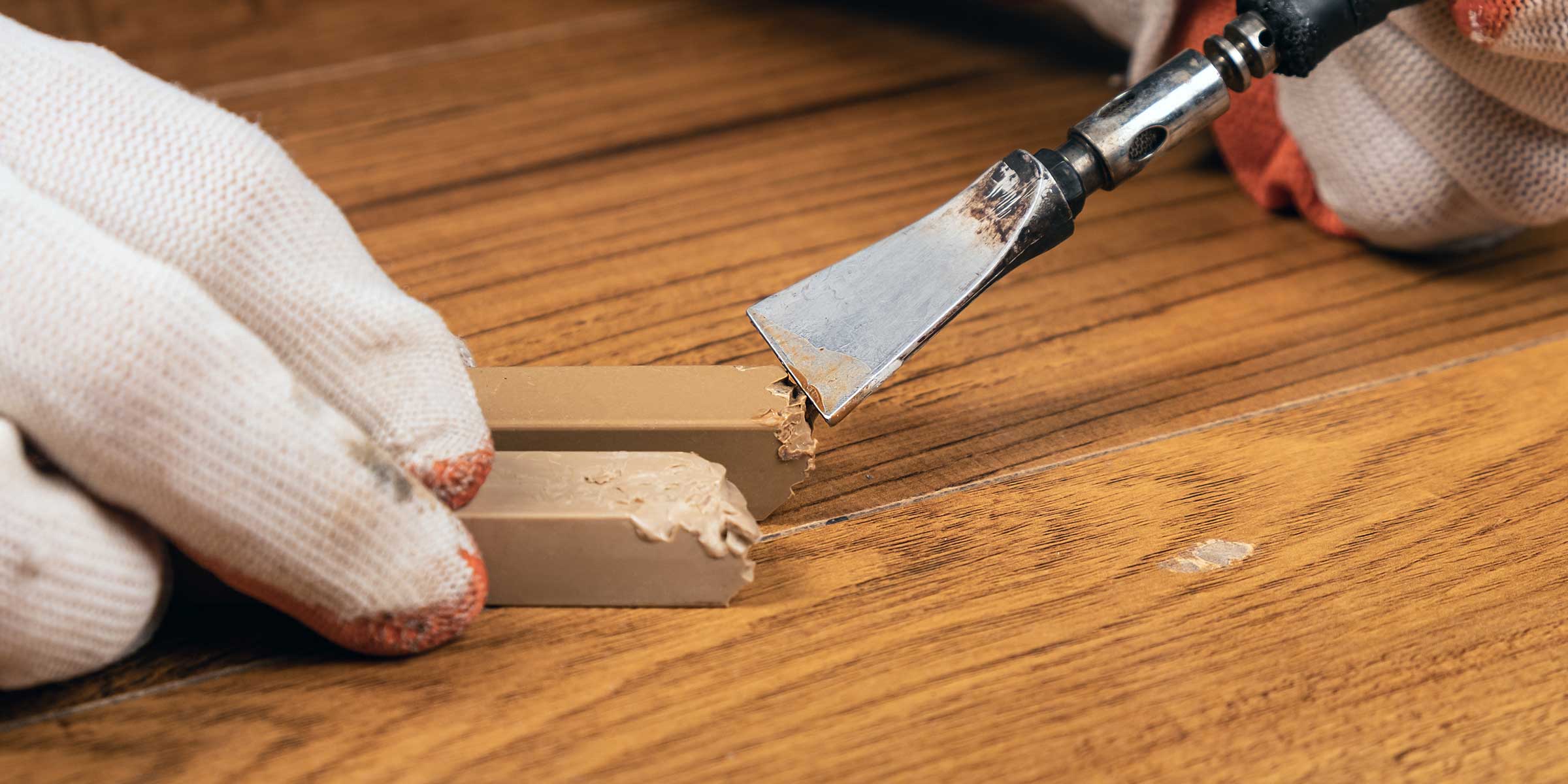 closeup of a person wearing gloves and repairing wood floor with a wood repair spatula kit