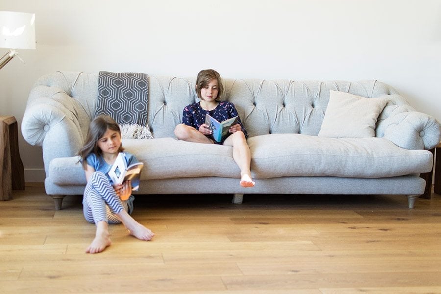 two little girls reading on a grey couch, light oak wood flooring in the foreground