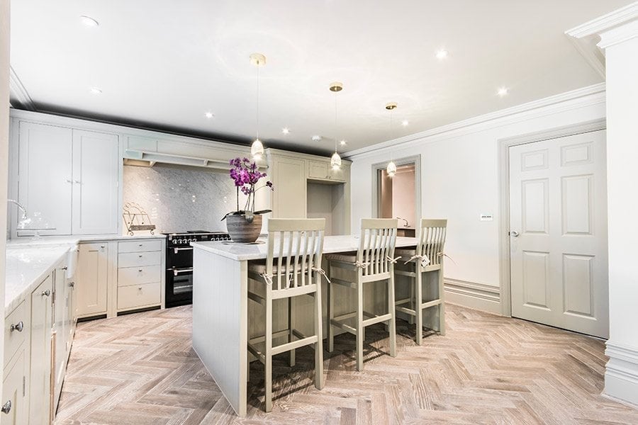 Parquet herringbone pattern in a light and airy modern kitchen, with a purple orchid flower pot on the middle island