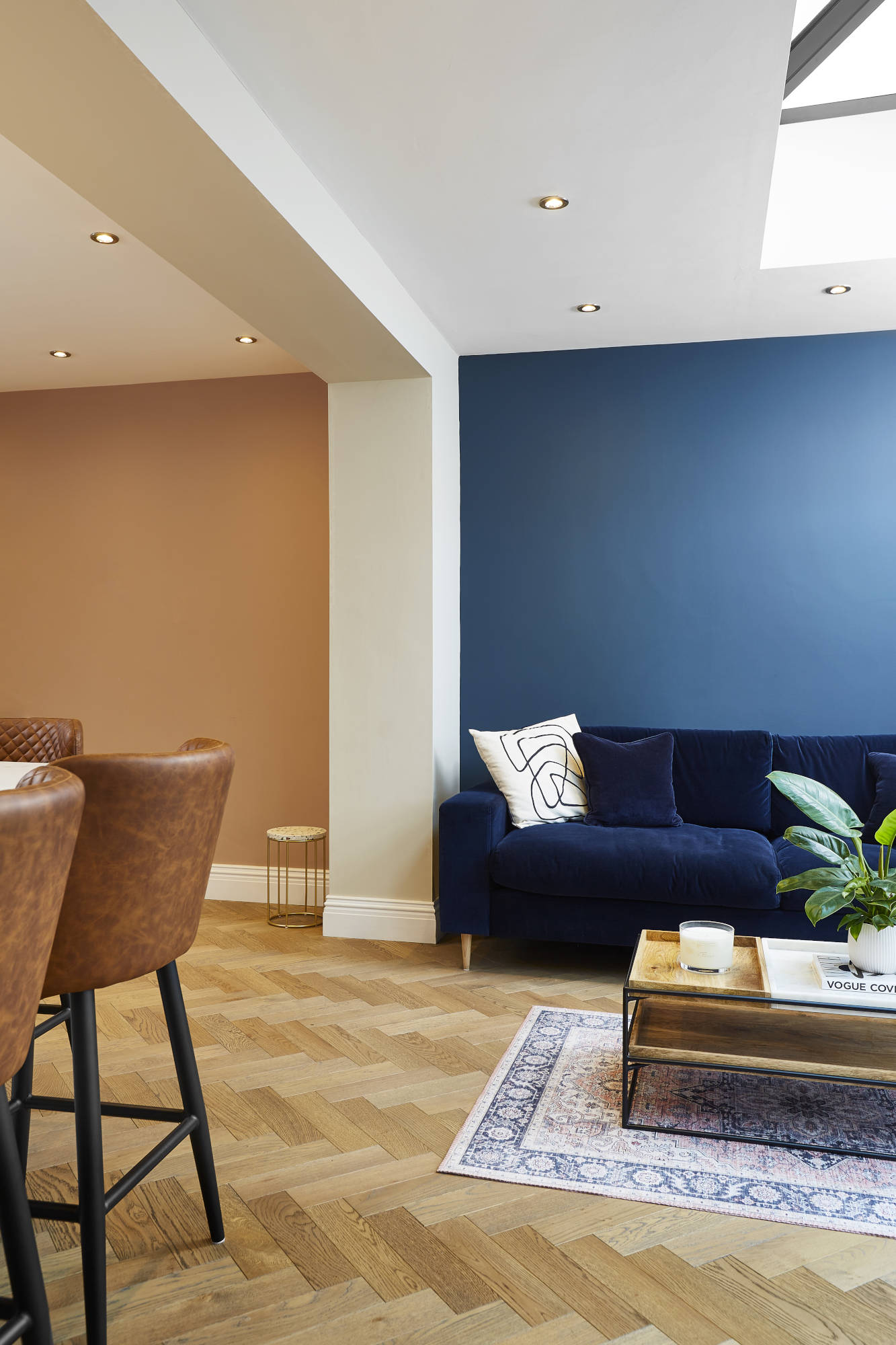 warm and inviting herringbone oak floors covering an open plan dining room and living room. Walls are painted warm coral and midnight blue