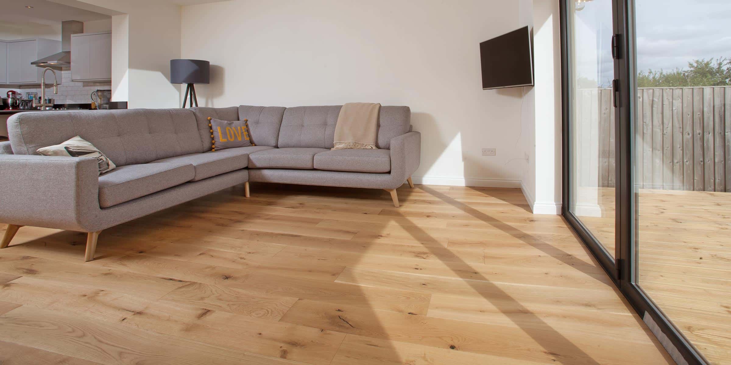 oak wood floors with a grey sofa leading to a patio behind glass paned doors