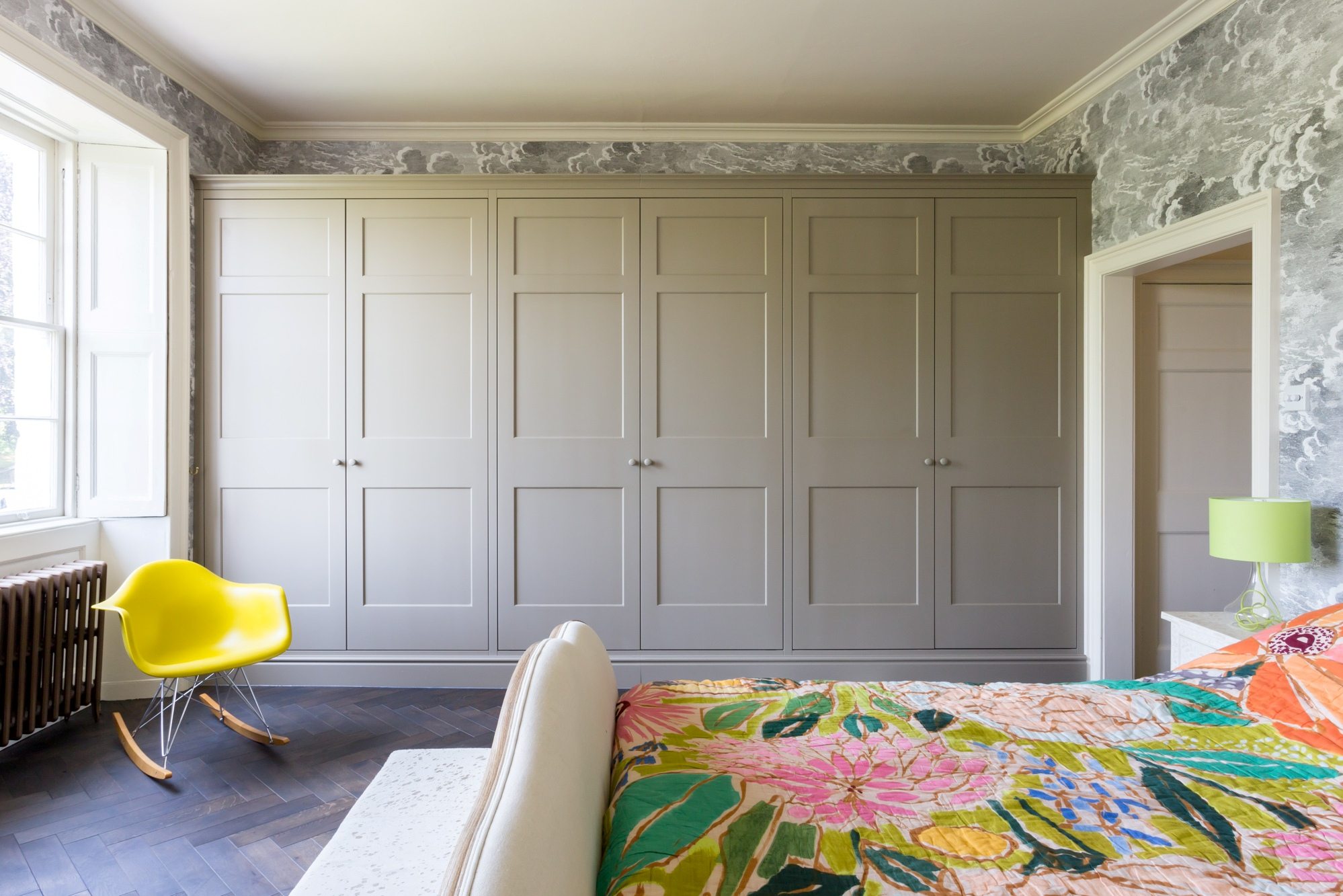 a dark herringbone wood floor in a bedroom with a fitted closet, bright yellow rocking chair, and bright duvet