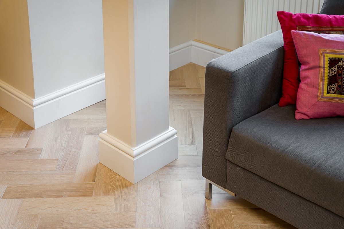 close up of herringbone wood floors with the corner of a grey couch