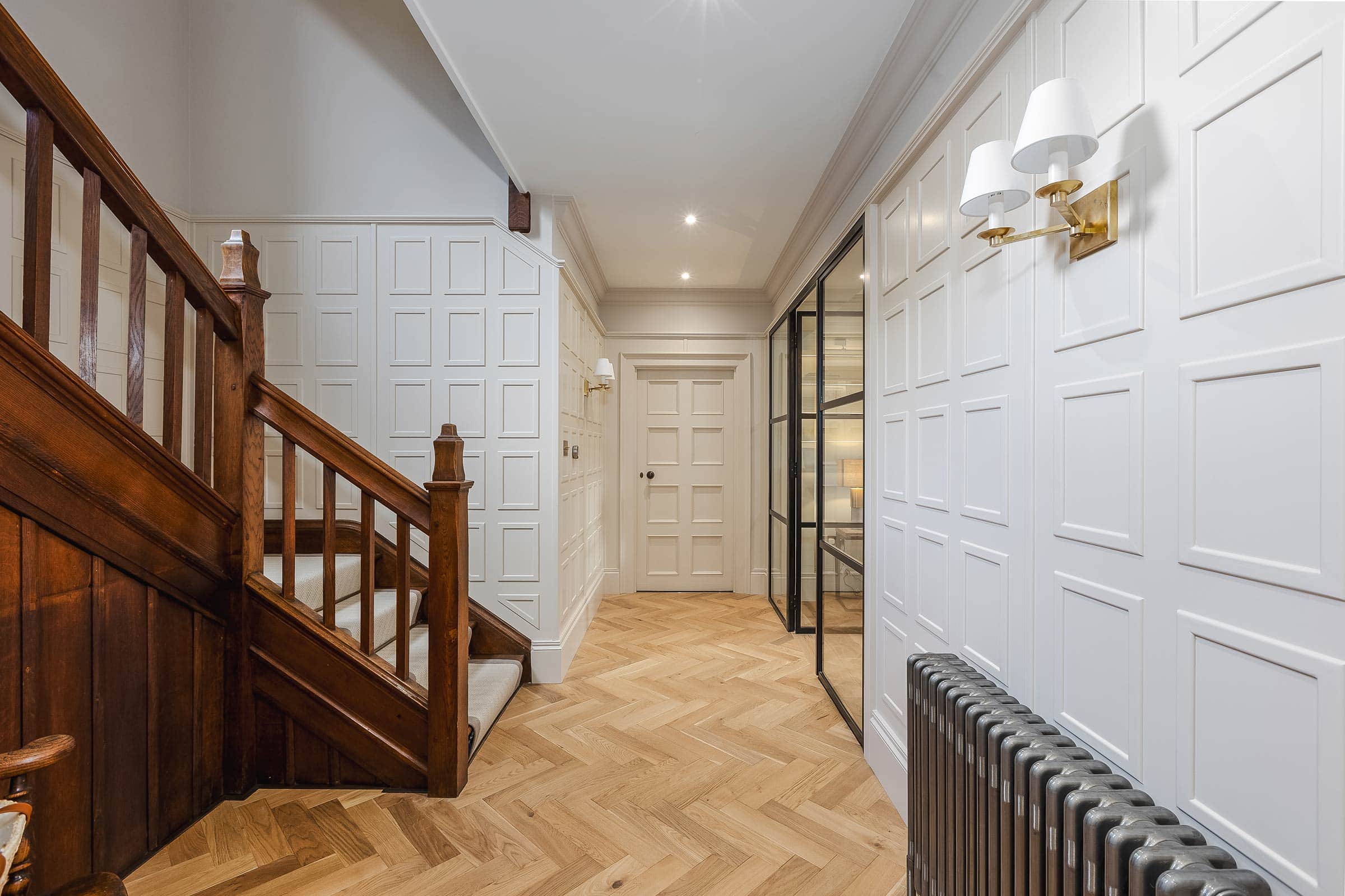 herringbone wood floors in a hallway entrance, with a wooden staircase and white walls