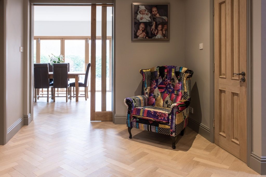 herringbone wood floors in a hallway with a colourful velvet armchair