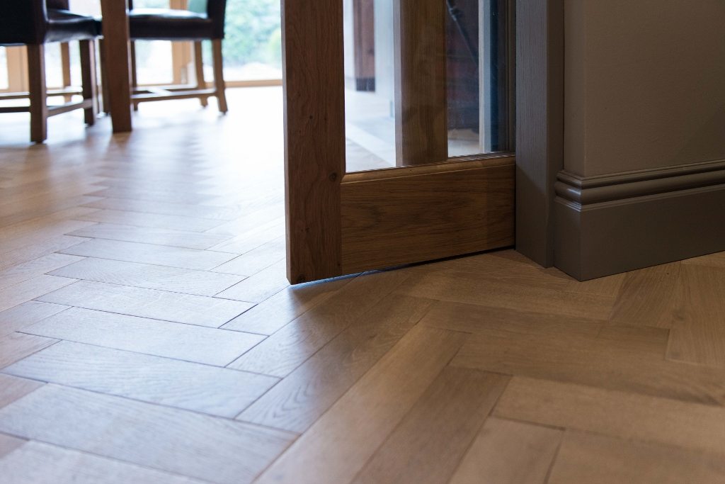 close up of herringbone wood floors with an open glass paned door