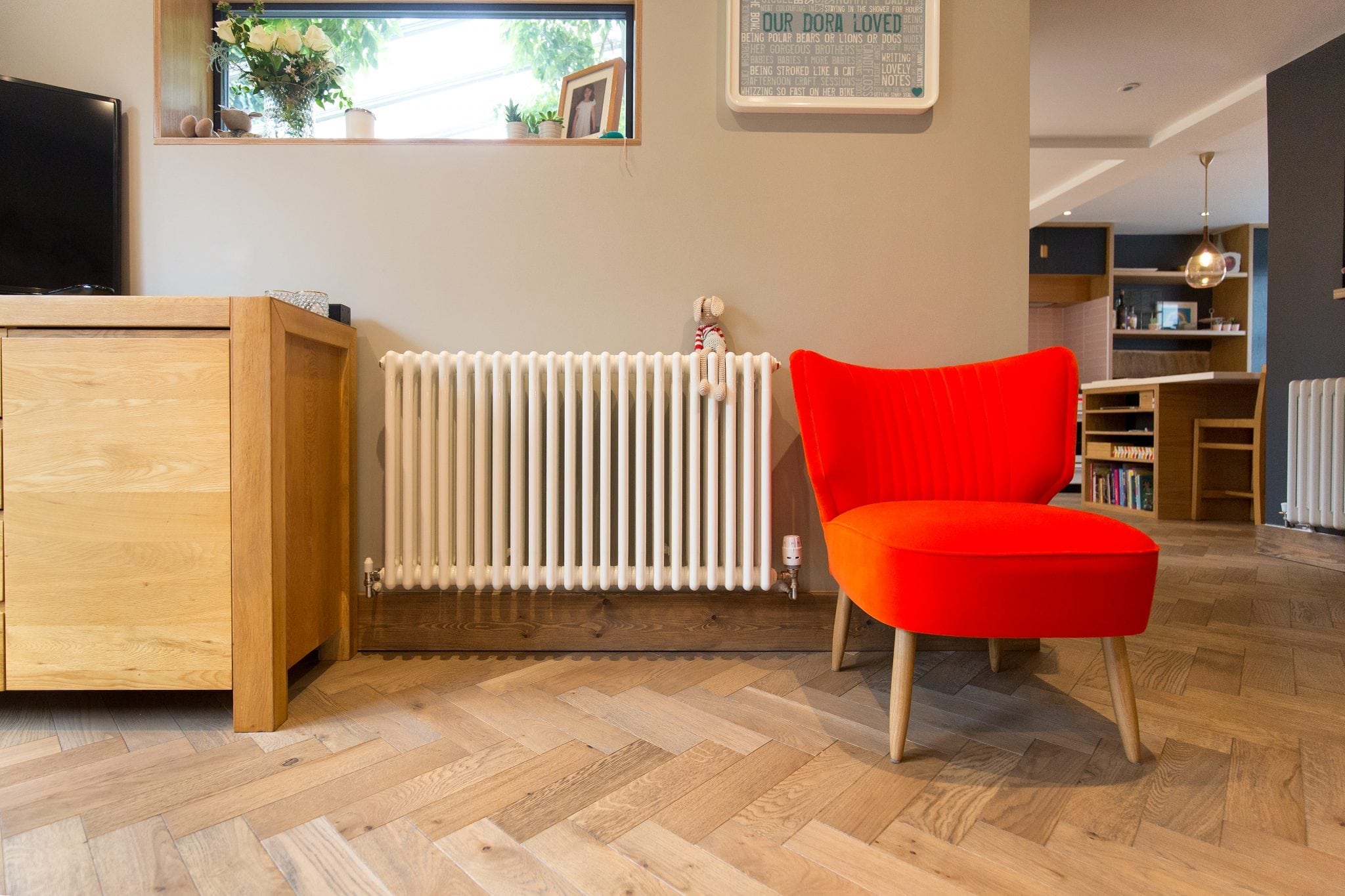 herringbone wood floors with a wood cabinet, white radiator and bright red chair