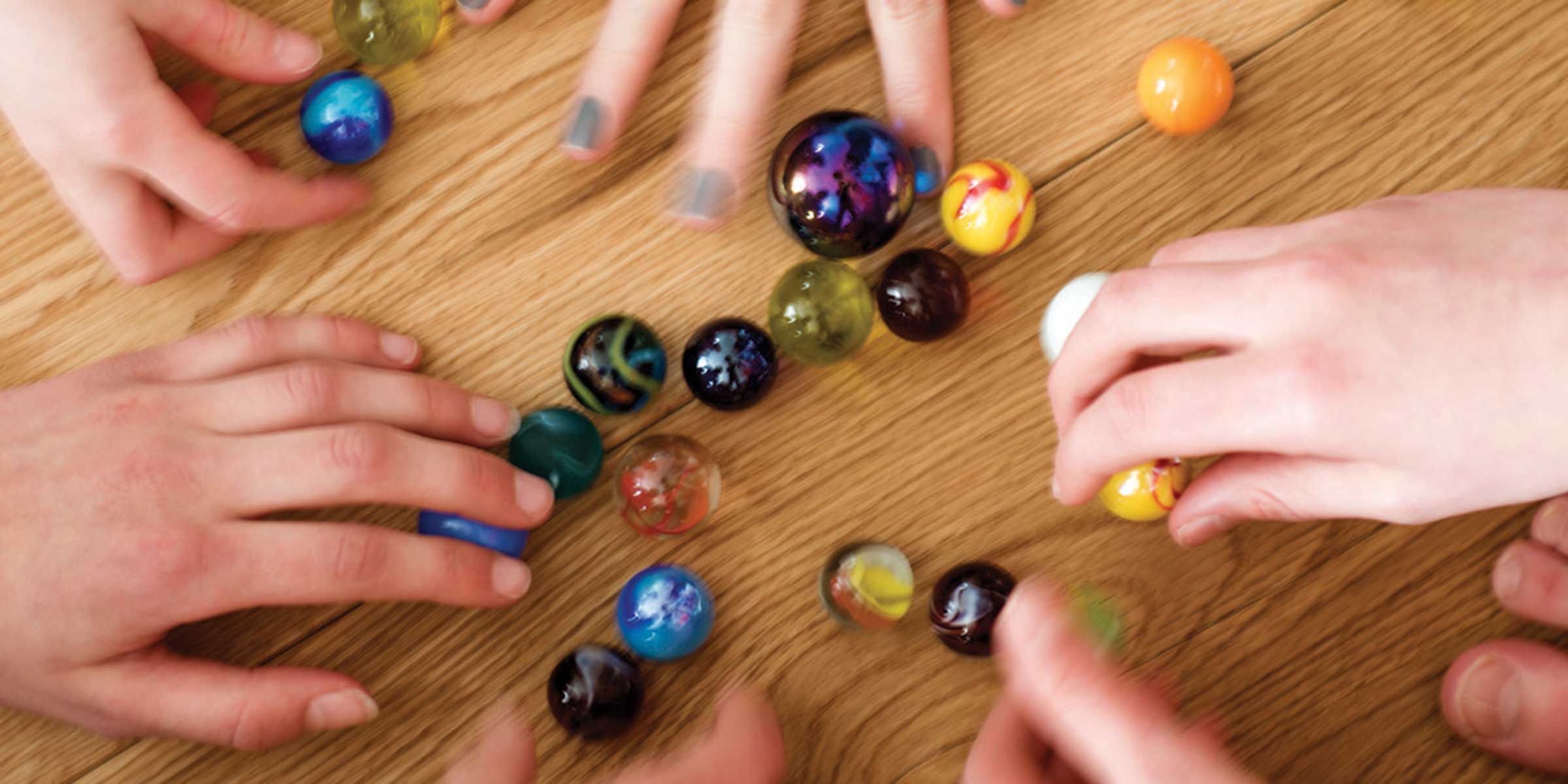 Multi coloured marbles on a wood floor with hands taking a marble