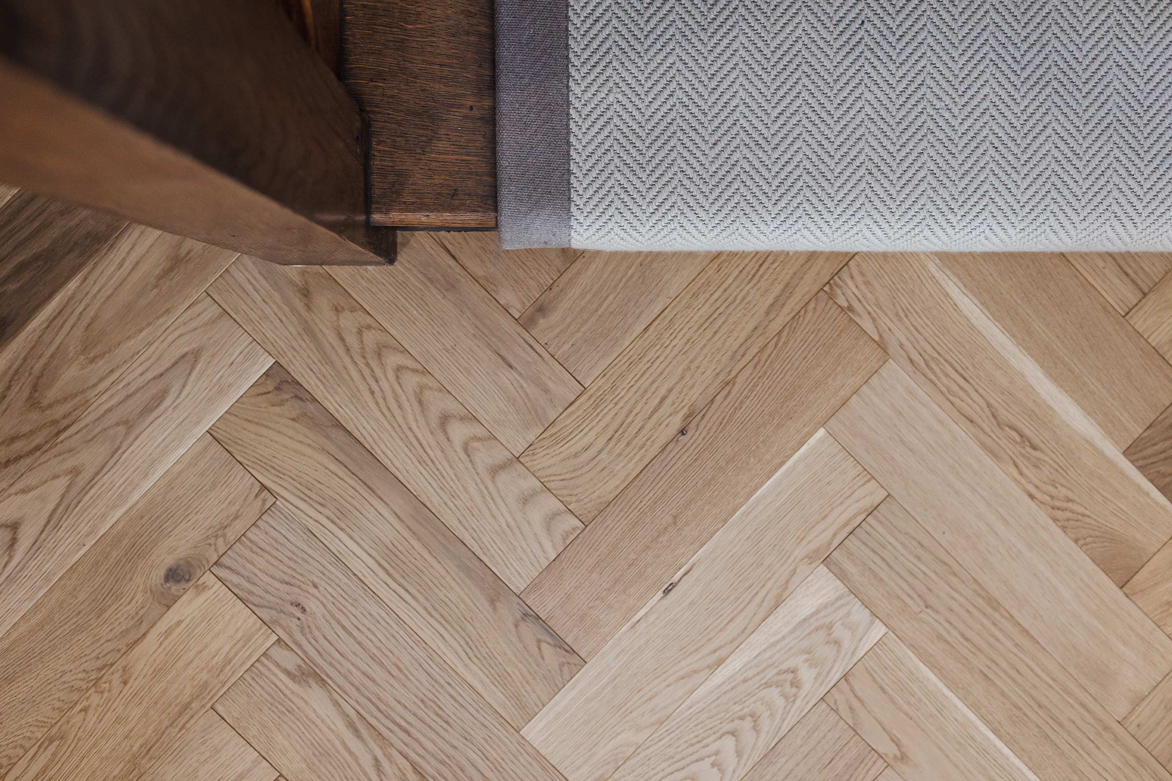 close up of herringbone wood floors at the base of a staircase