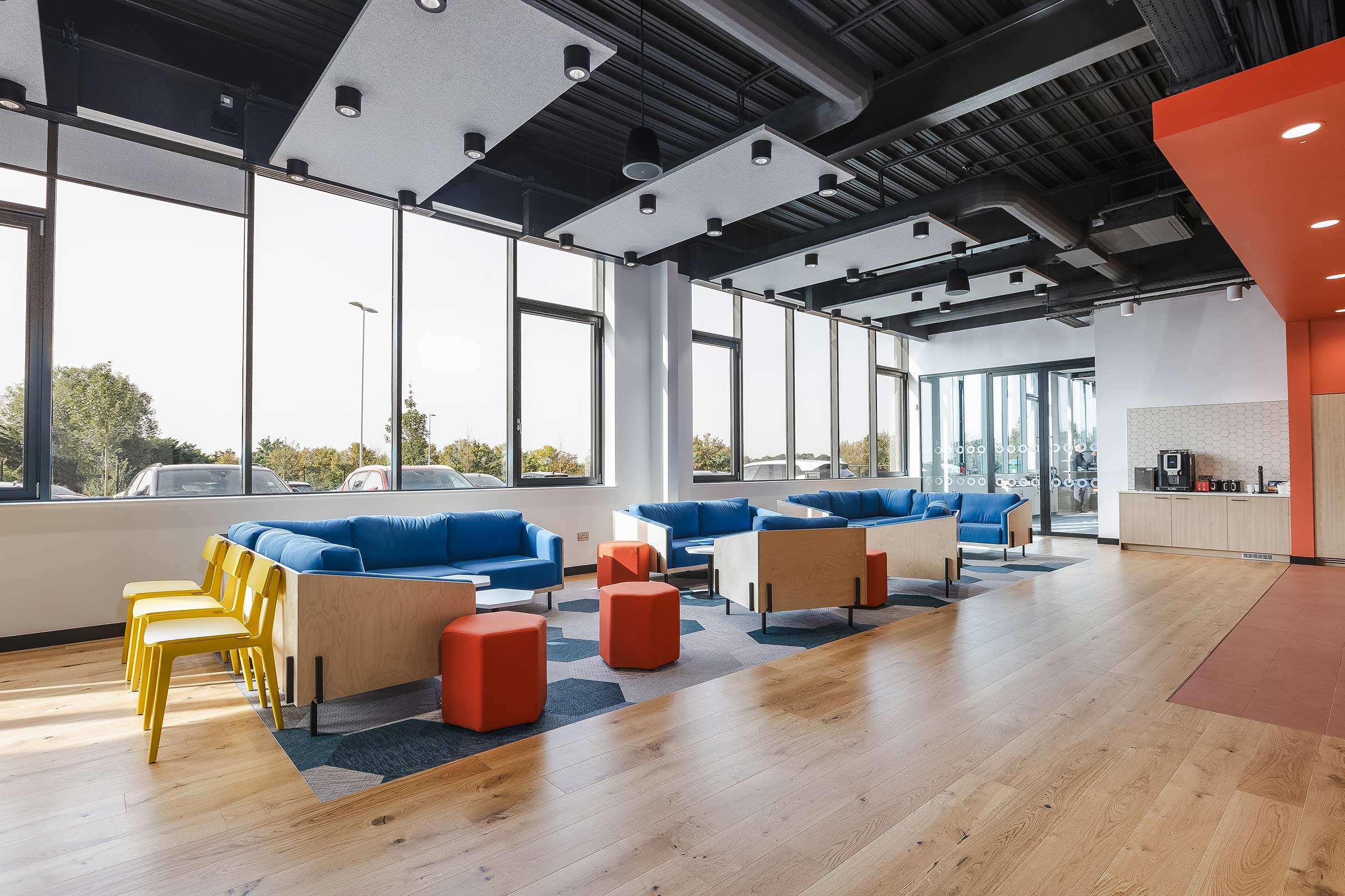 wood floors in a large and bright communal space with bright blue and orange cushions