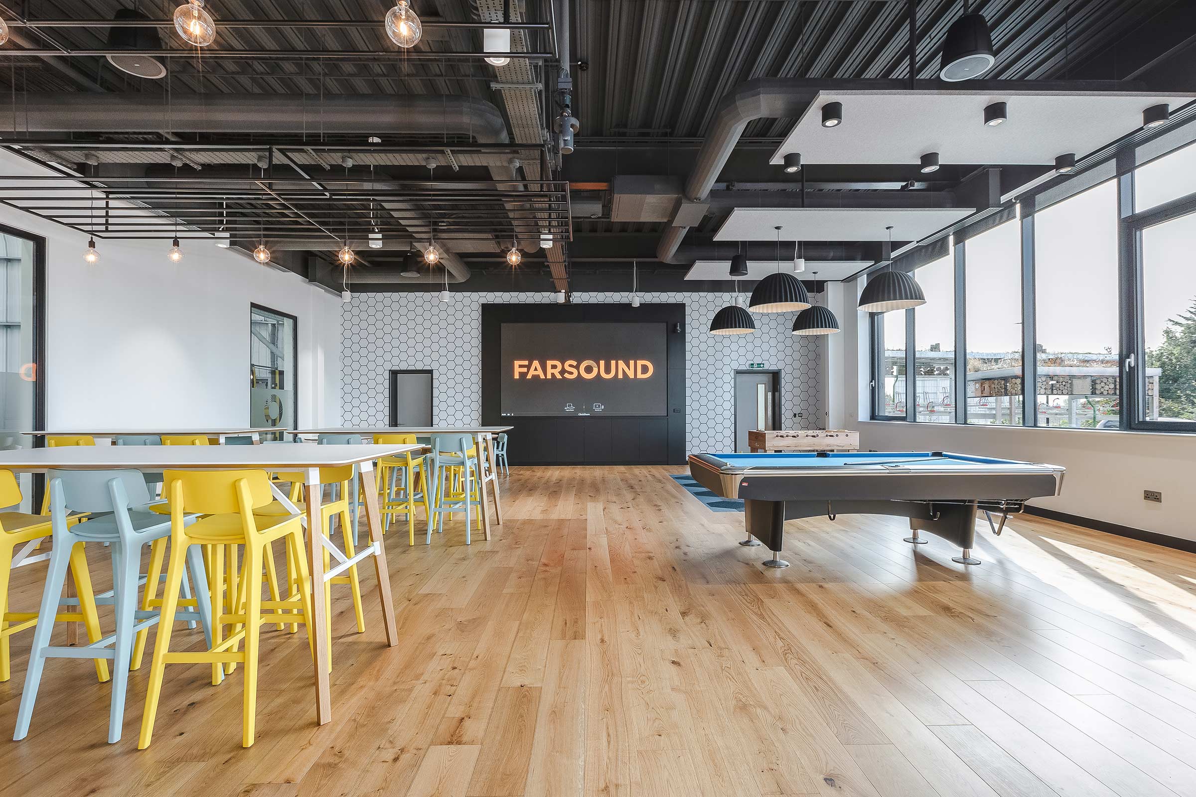 wood floors in a large communal space with yellow chairs and a pool table