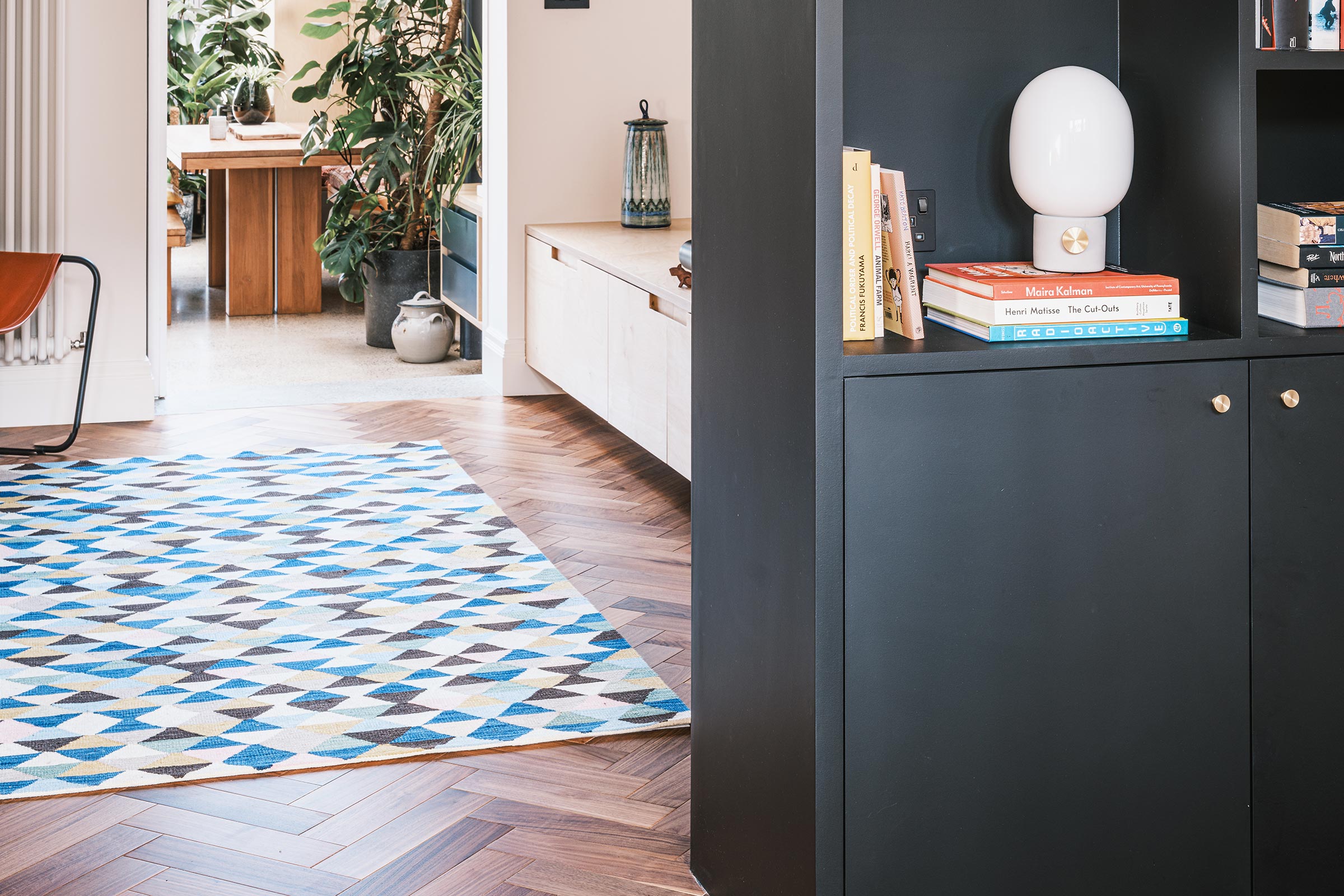 herringbone wood floor in a light and airy modern living room with a rug and dark blue shelves