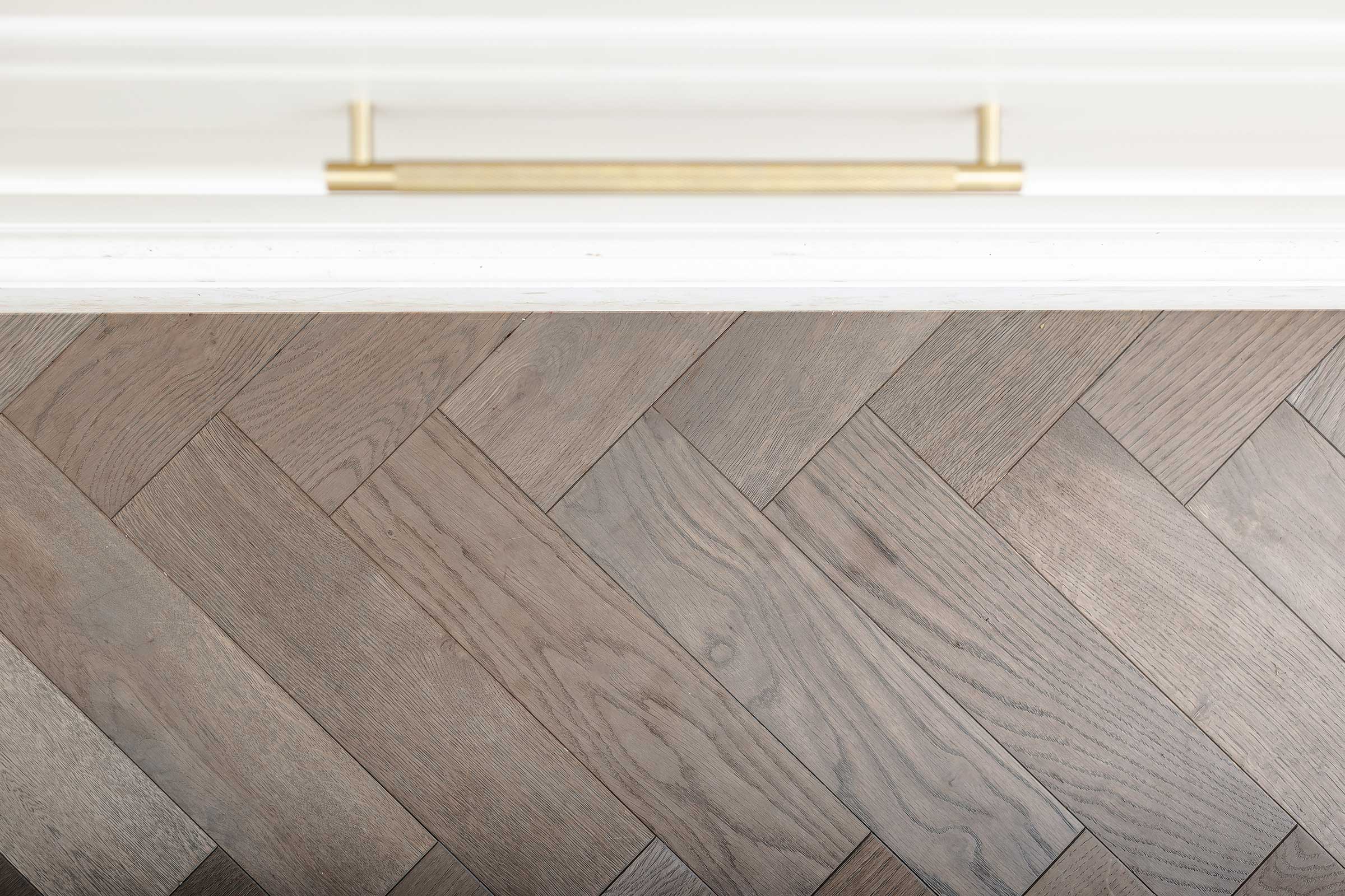 close up of a white drawer and brass handle with herringbone wood floors