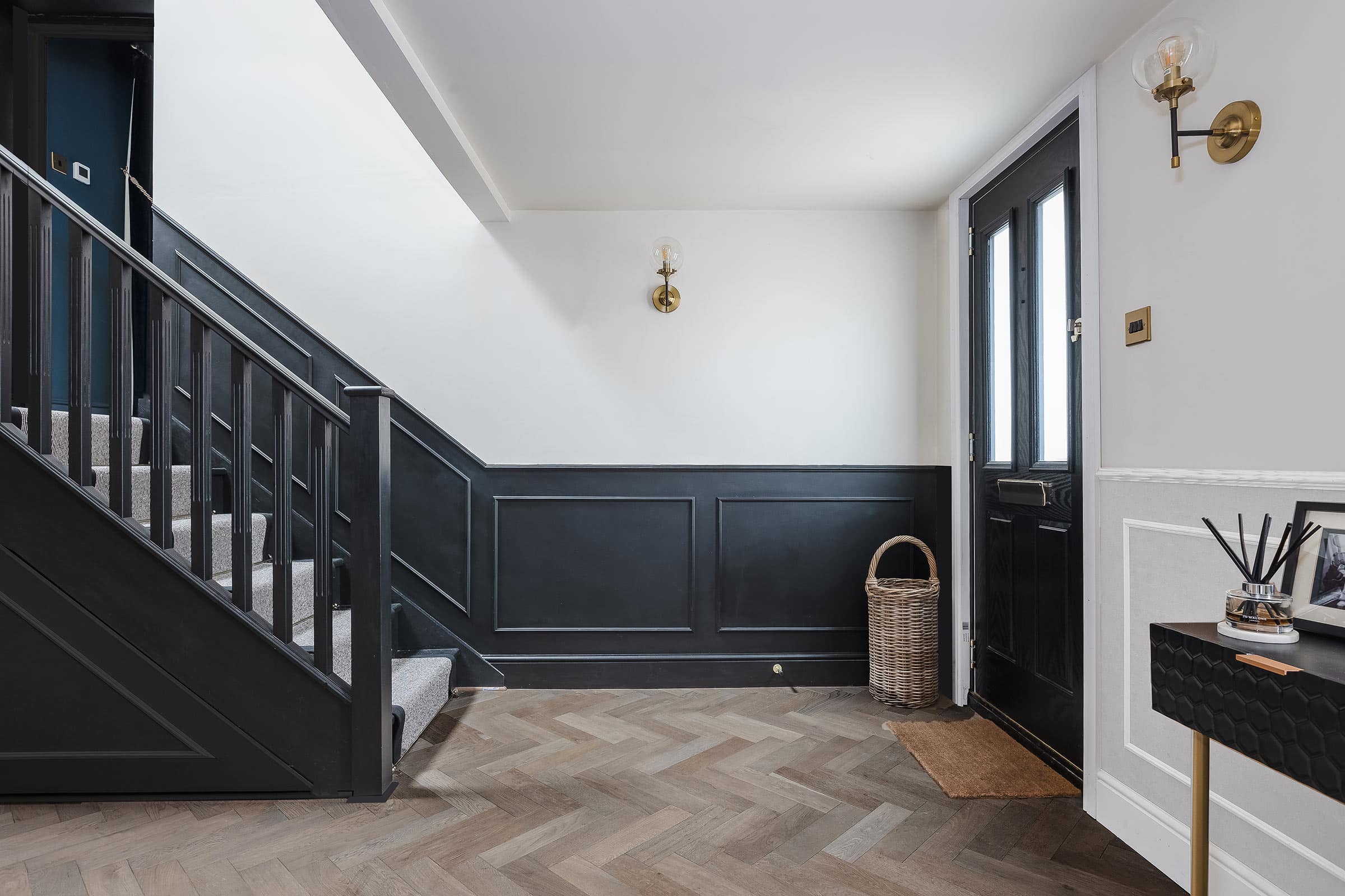 herringbone wood floors in a hallway with a stair case, navy and white walls